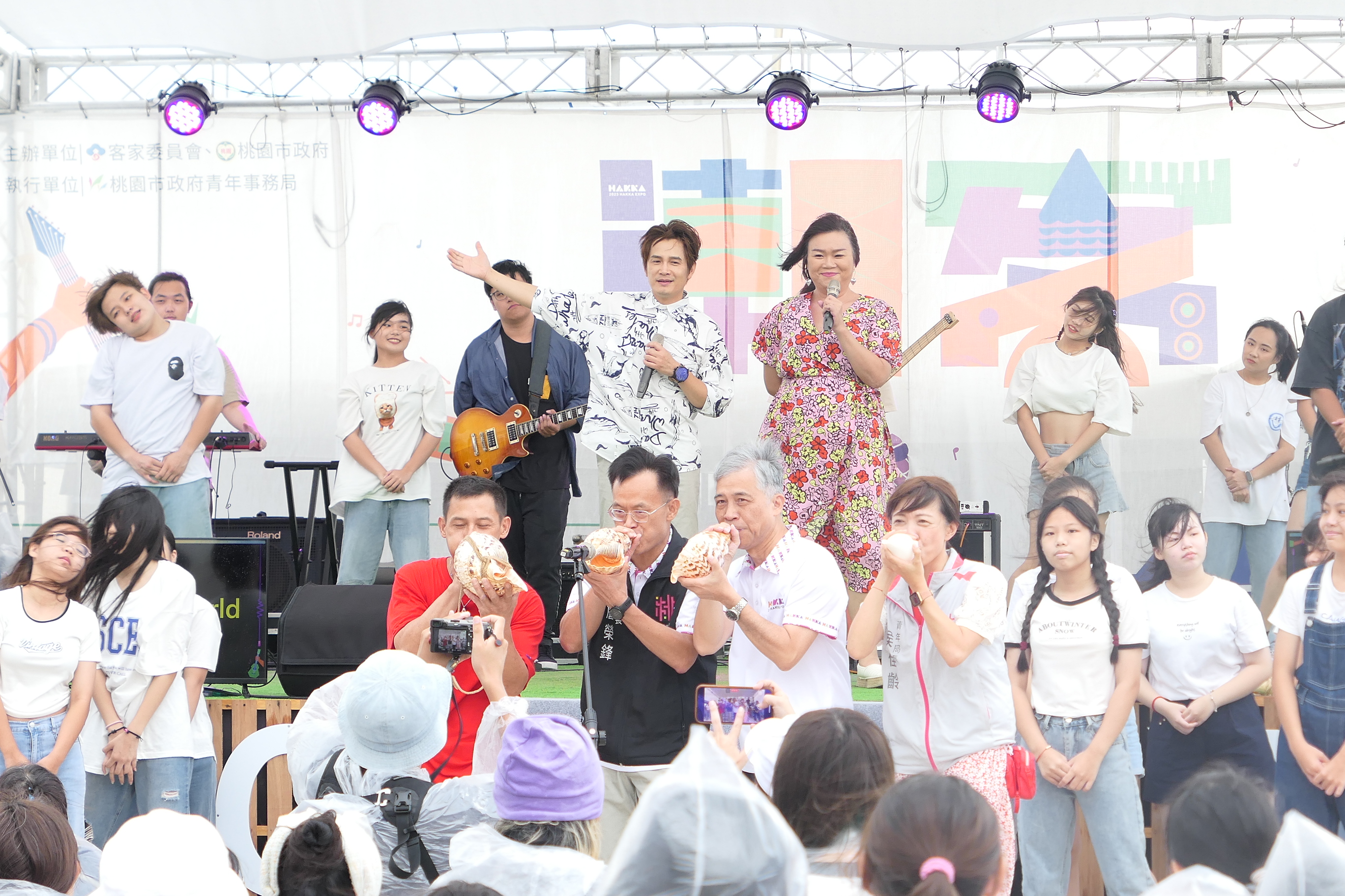 圖1客家金曲歌王羅文裕領唱世客博主題曲〈Hakka New World〉，並由客家委員會副主委范佐銘、歕嘟達人許立志、桃園市政府秘書長詹榮鋒及青年局局長侯佳齡共同吹響海螺.JPG